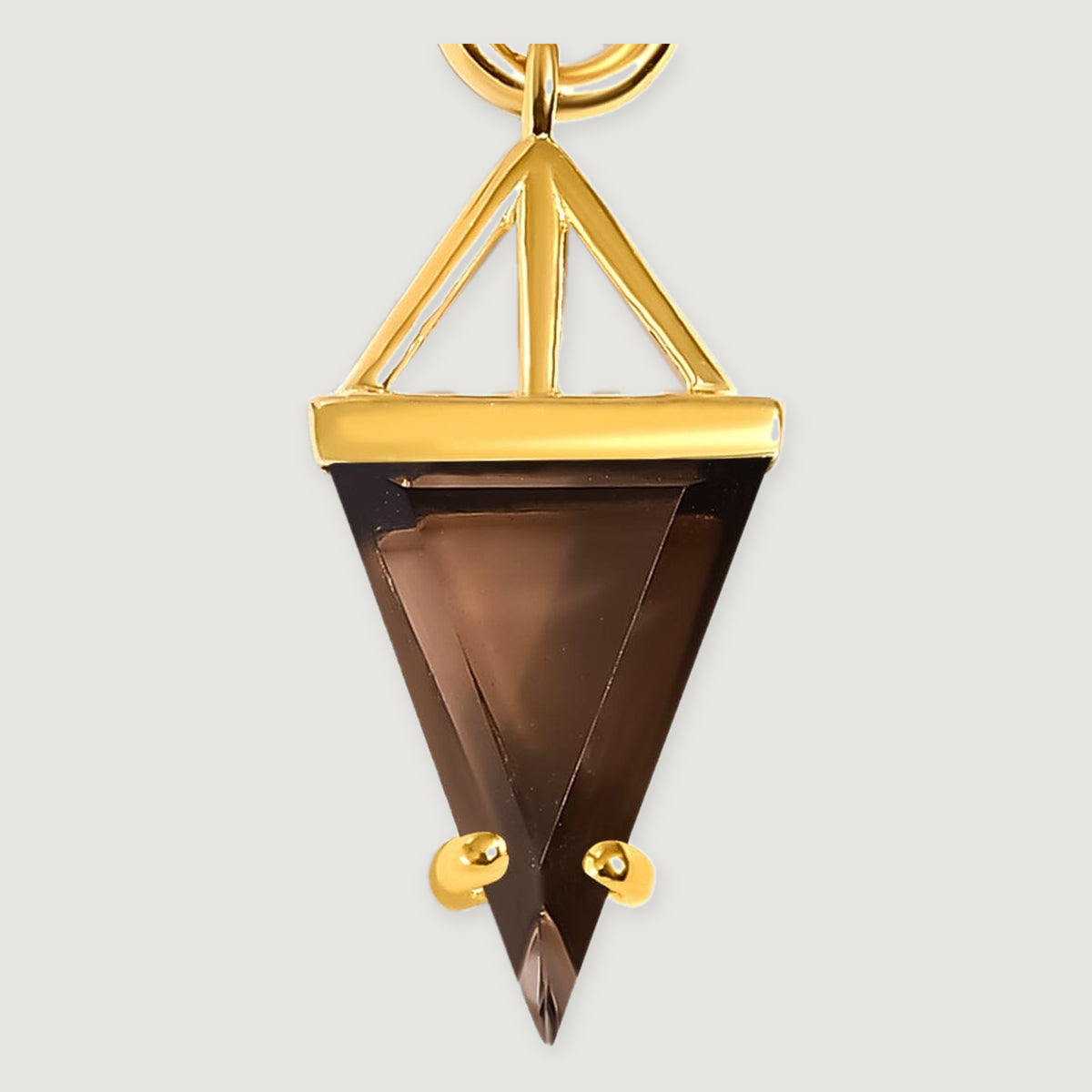 A close view shows the smoky quartz triangle, open gold support and two rounded gold prongs against a pale gray background.