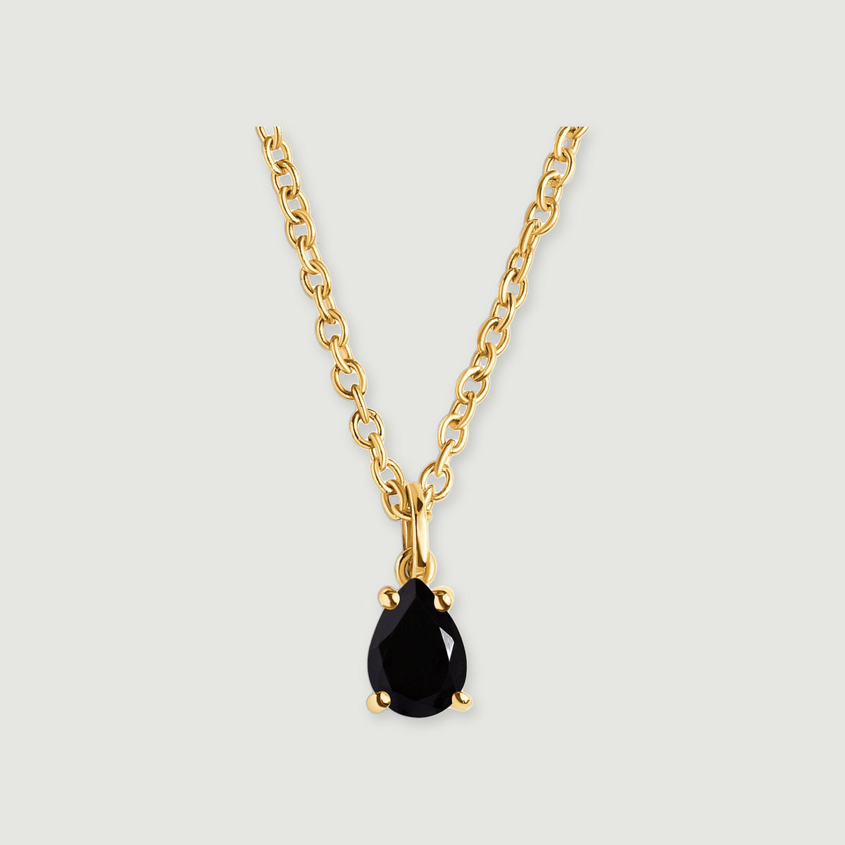 A pear-shaped black obsidian pendant hangs from an oval-link yellow gold-colored chain on a light gray background.