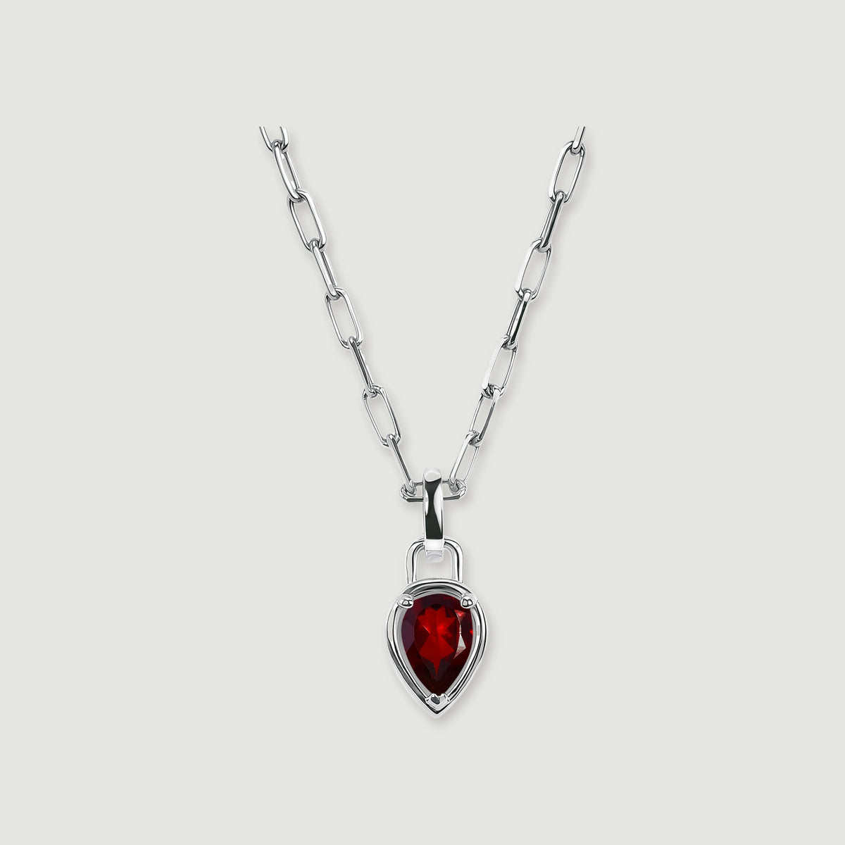 A silver-tone rectangular-link chain holds a deep red pear-shaped pendant against a softly shadowed gray surface.