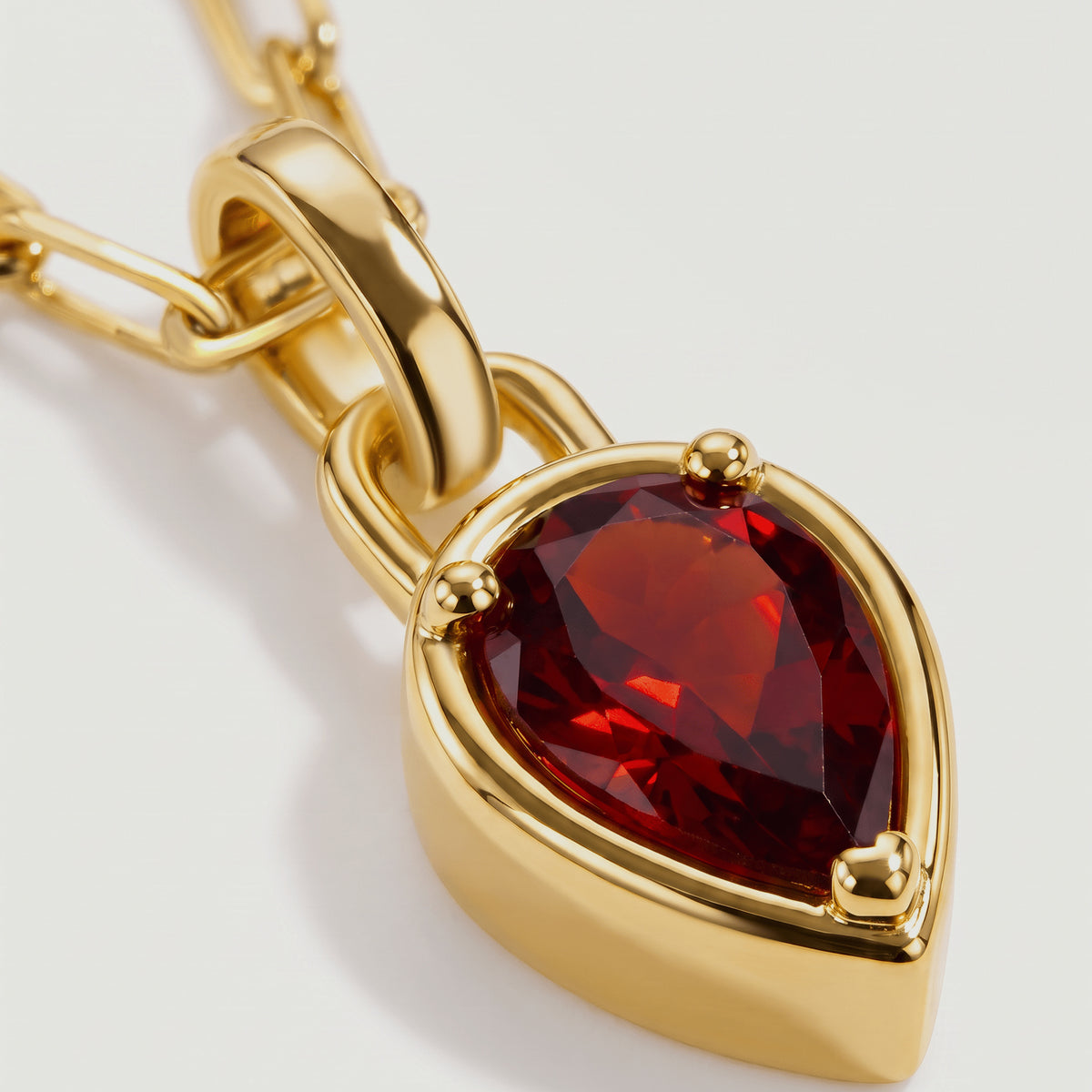 A close view reveals the red gemstone facets, rounded gold-tone prongs, and curved pendant bail.