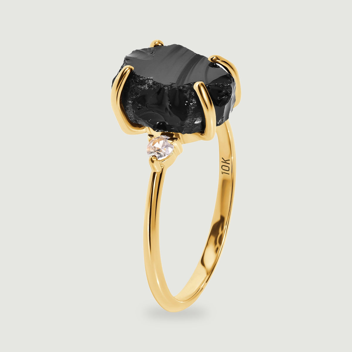 A side view shows the raised black stone, a clear side stone, and the slim yellow gold band.