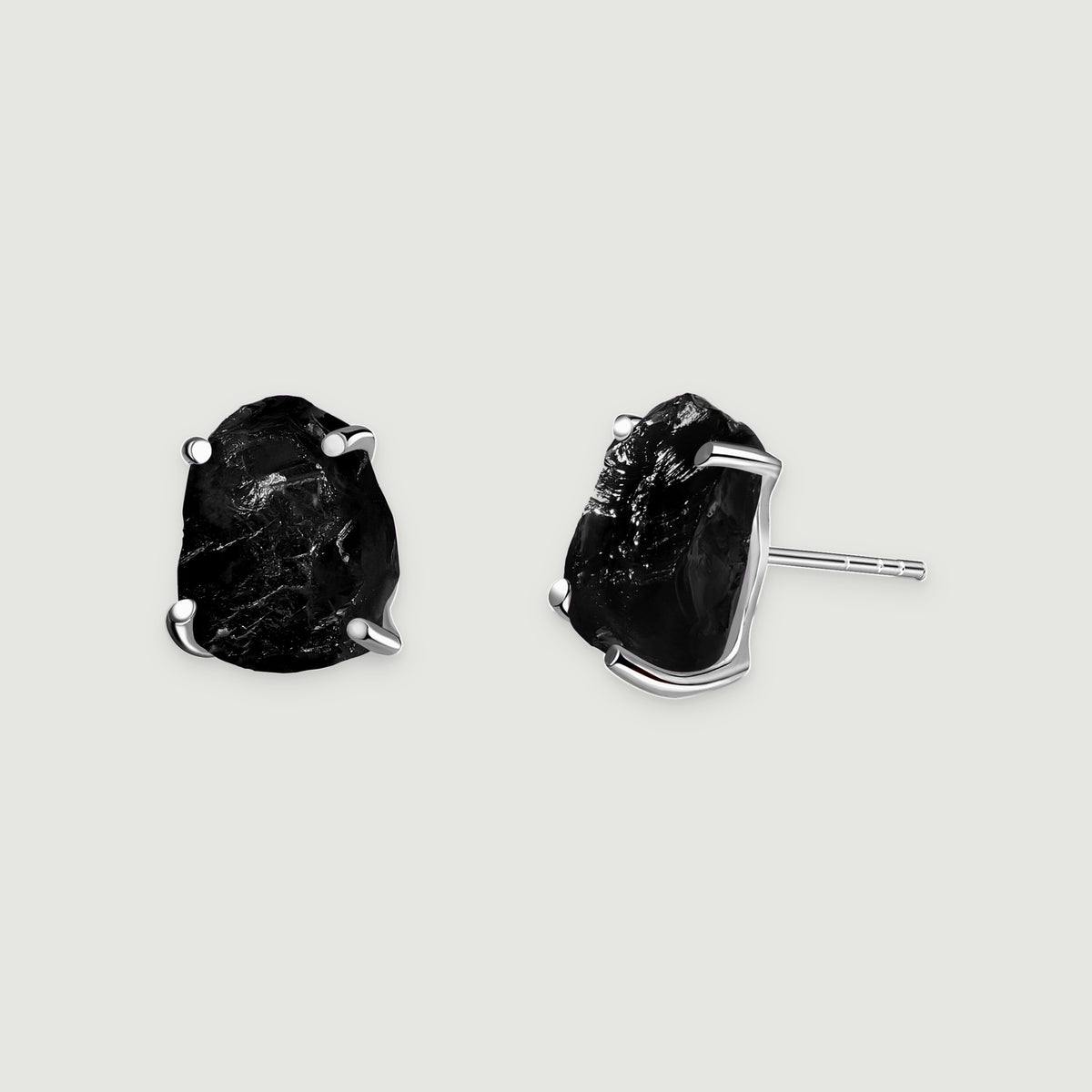 A pair of black obsidian studs displays silver prongs and a straight earring post on a pale gray background.