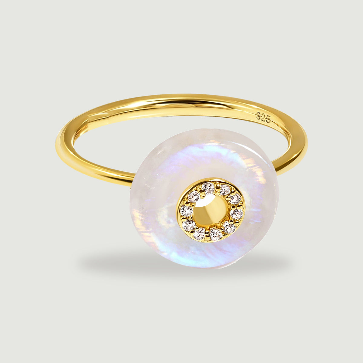 A yellow gold ring with a round iridescent moonstone disc and a circle of clear stones on a light gray surface.