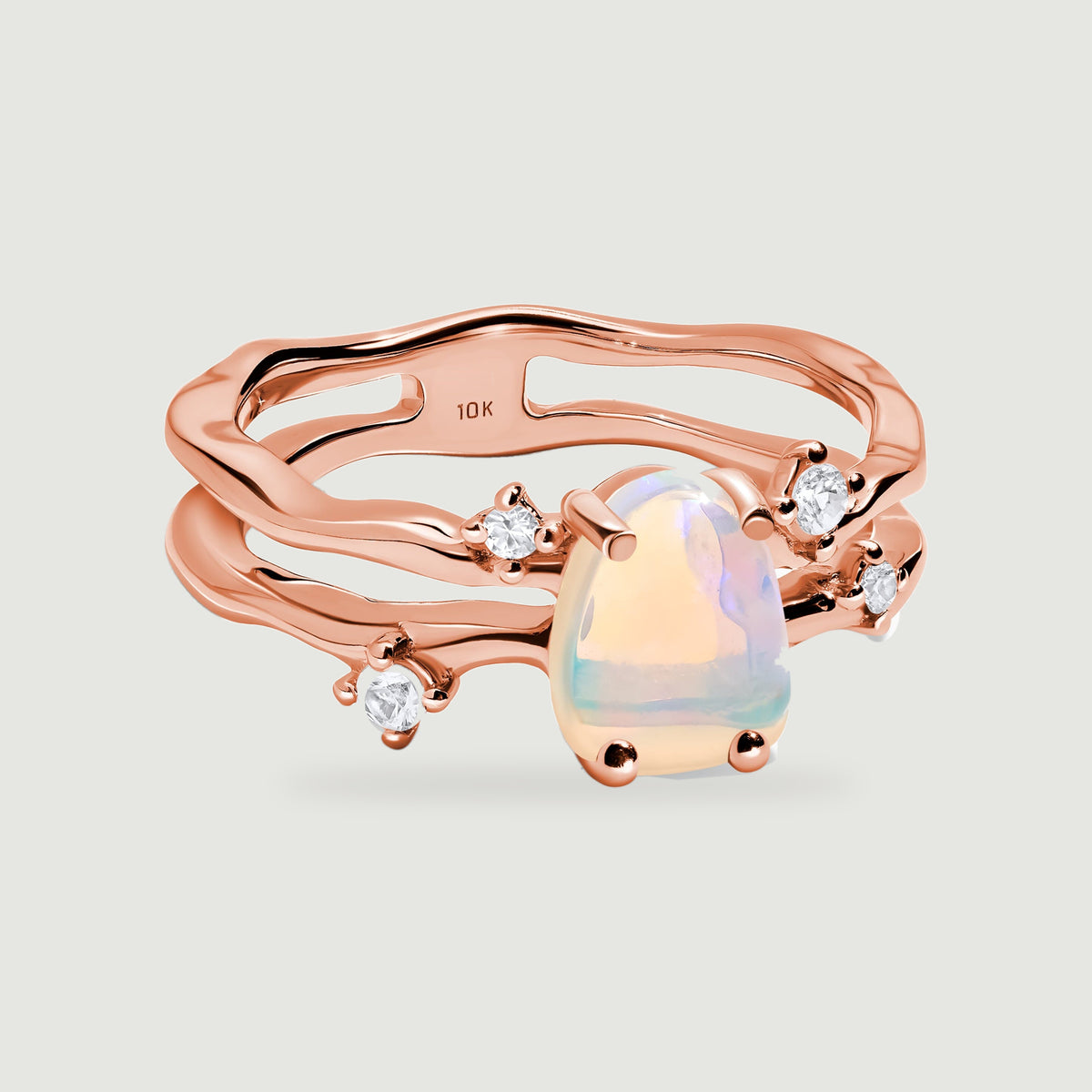 A rose gold ring has an iridescent opal, four round clear stones and a wavy double band.