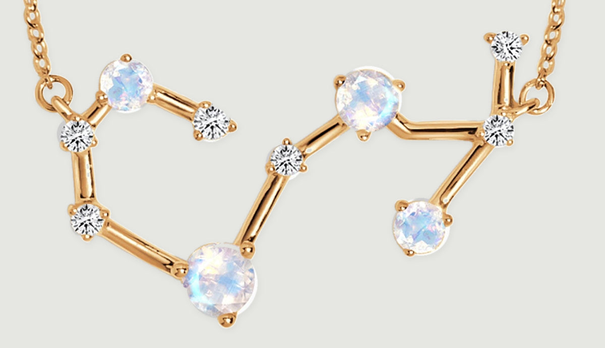 A close view shows pale faceted stones, bright clear accents, and gold bars forming an open angular pendant.