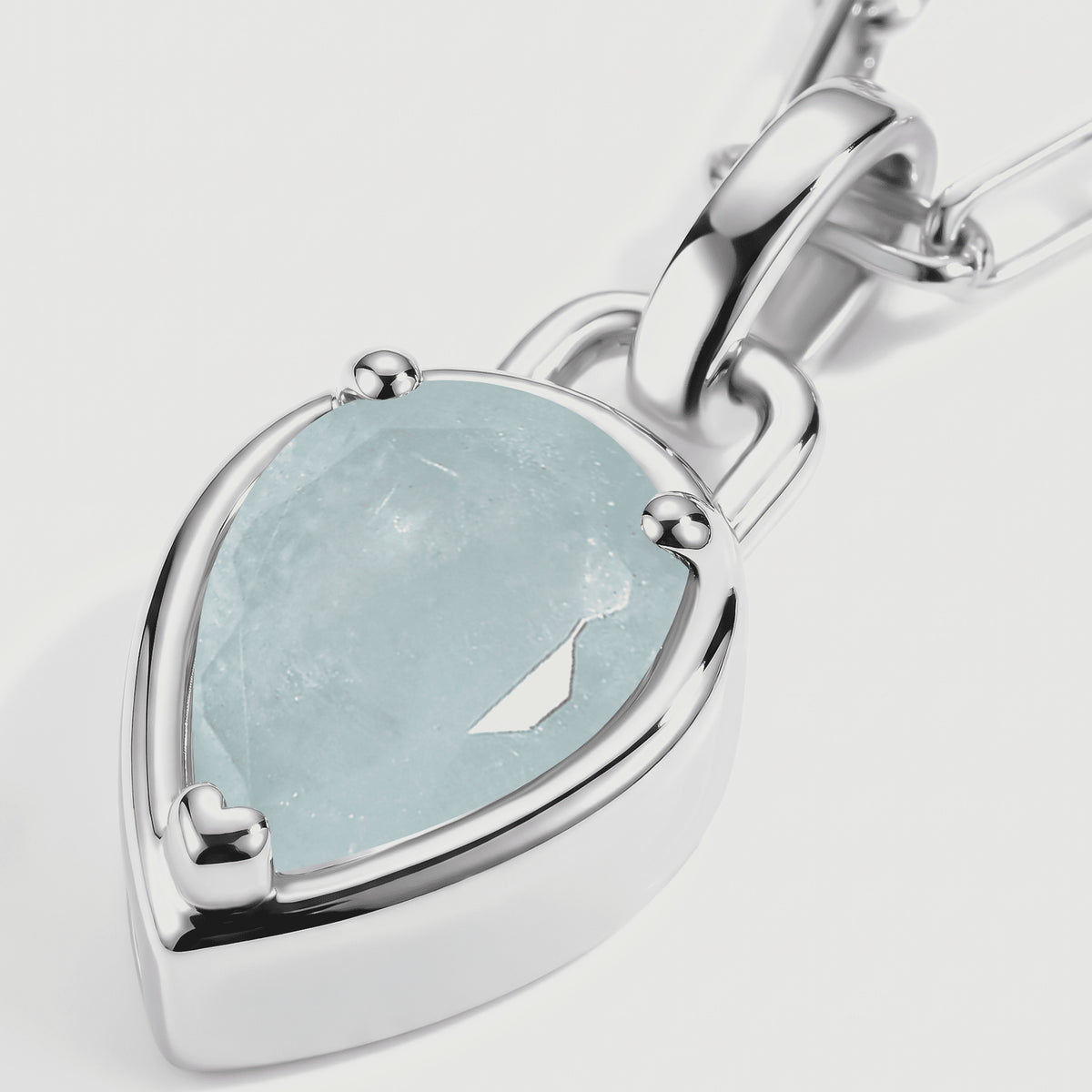 A close view shows the pale blue faceted stone, three polished prongs, and silver-colored pendant rim.