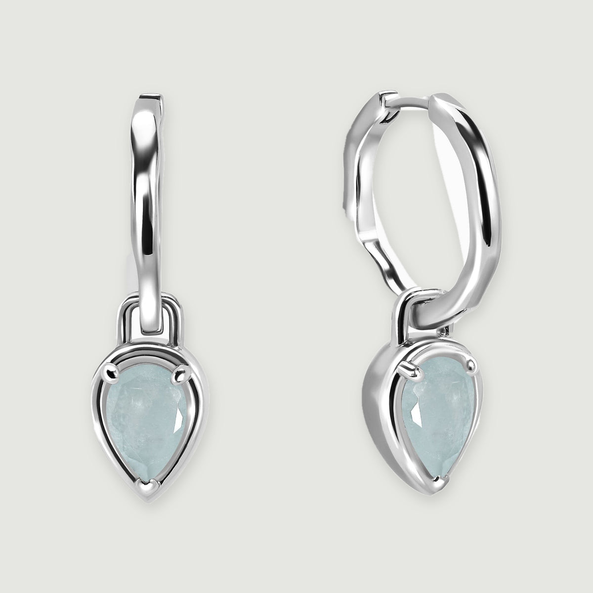 Two polished silver-tone hoop earrings with pale blue pear-shaped aquamarine drops rest on a light gray background.