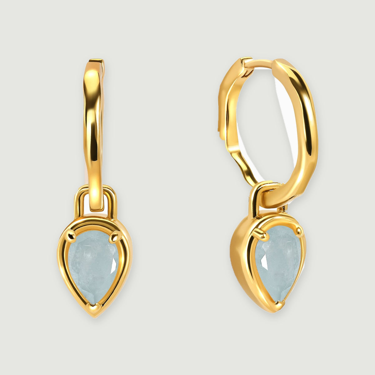 A pair of yellow gold-tone hoops with pale blue aquamarine drops is centered above soft shadows.