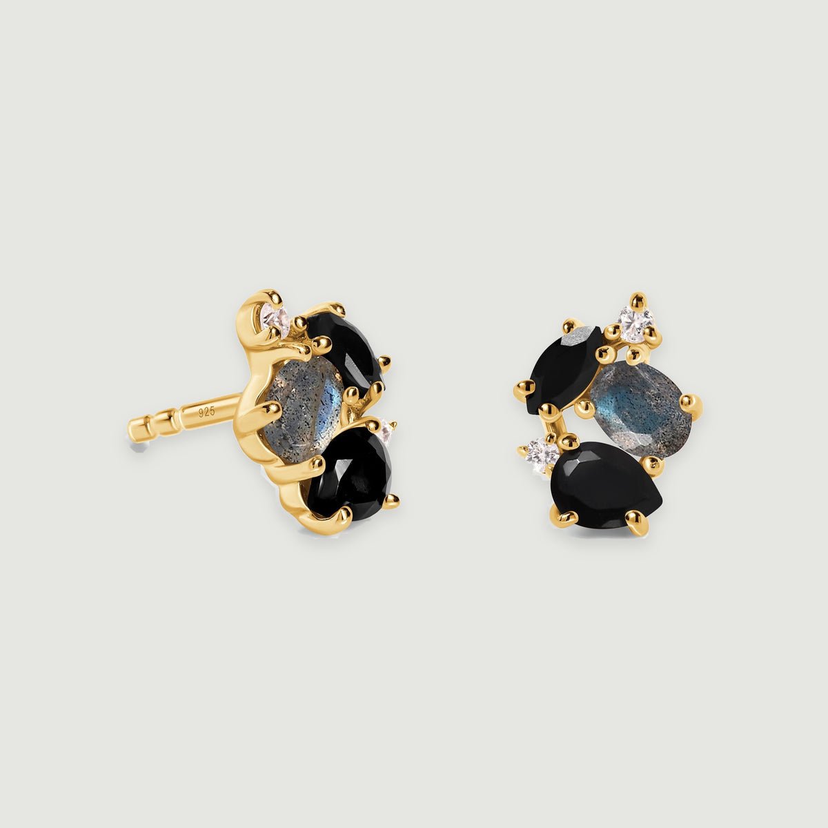 Two yellow gold vermeil stud earrings display black gemstones, oval blue gray stones and clear accents with soft shadows beneath them.