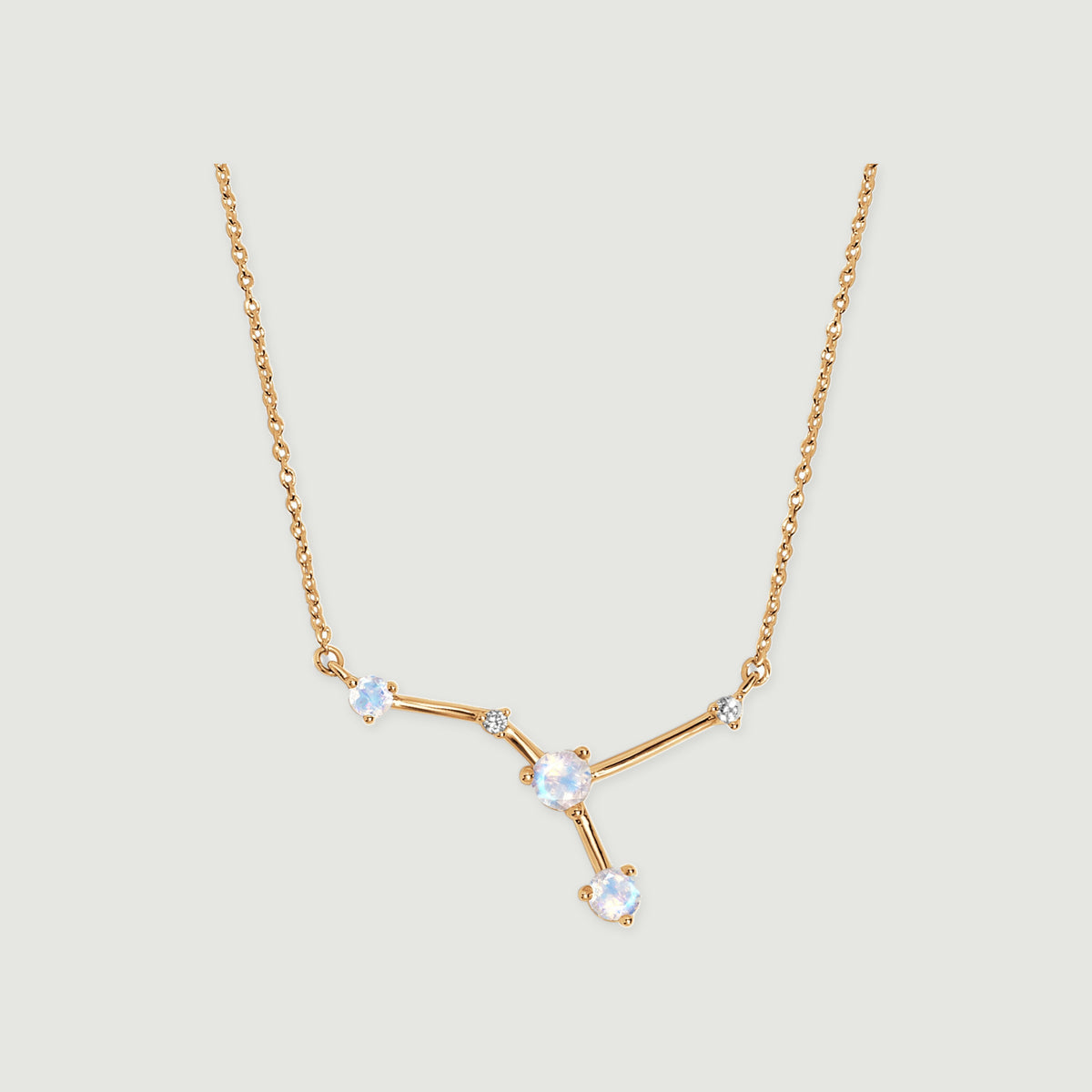 A yellow gold vermeil necklace has polished angular bars joining pale faceted stones against a gray surface.