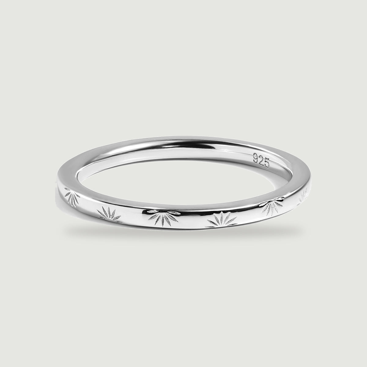 A polished silver band with radiating engravings rests on a light gray surface.