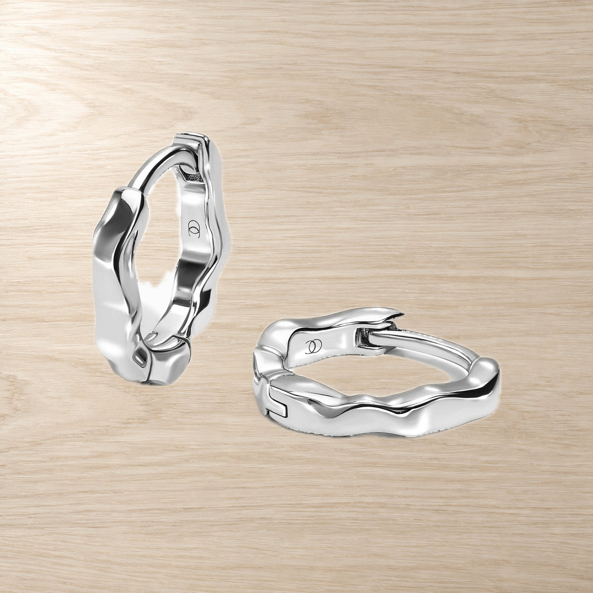 Pair of sculpted wavy hoop earrings displayed on a pale wood surface, showing hinged closures.