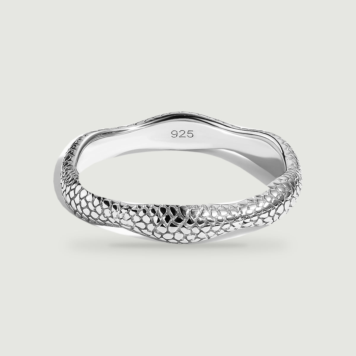A silver ring with a rippled edge and raised textured surface rests on a pale gray background.