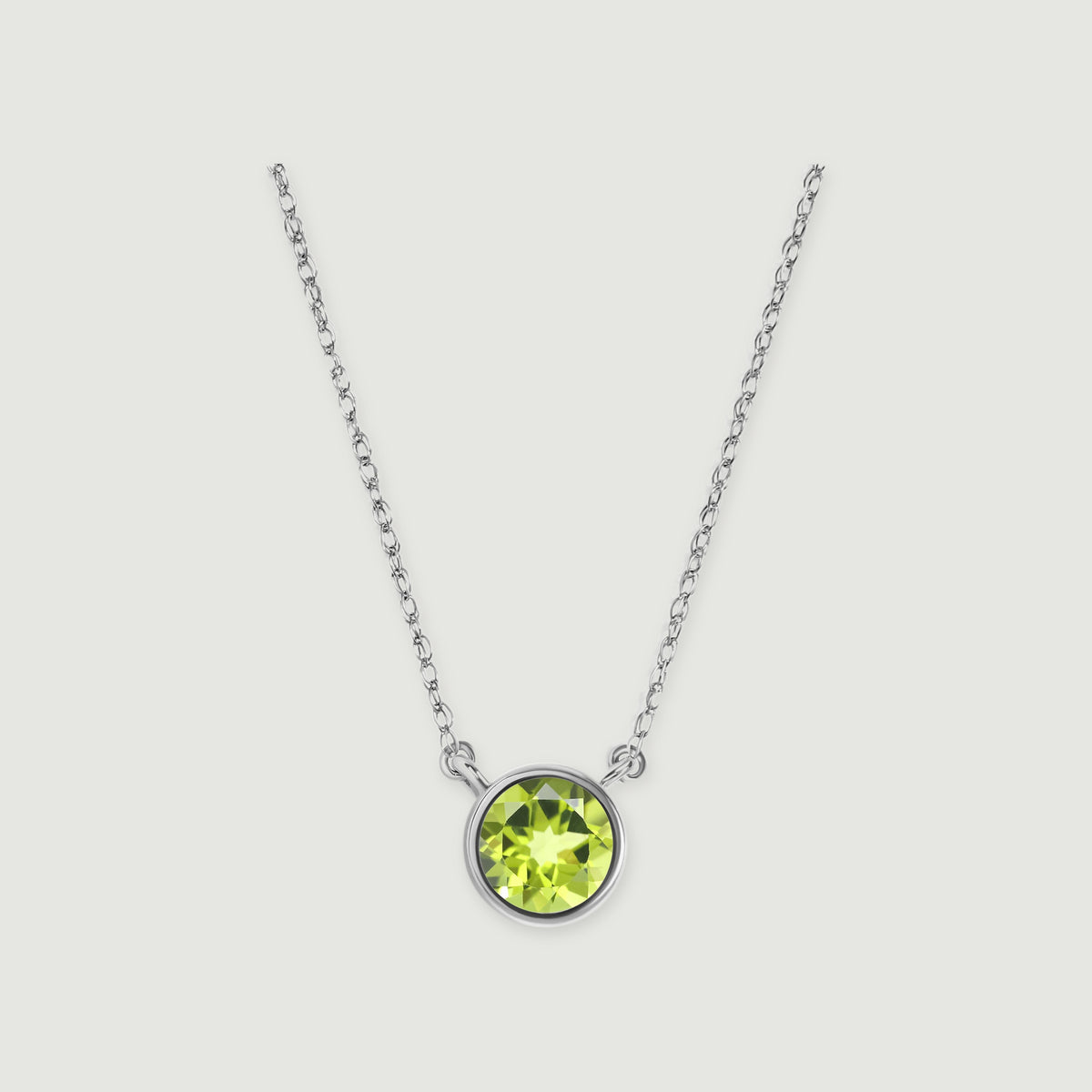 A white gold chain meets a circular bezel holding a faceted green peridot against a pale gray background.