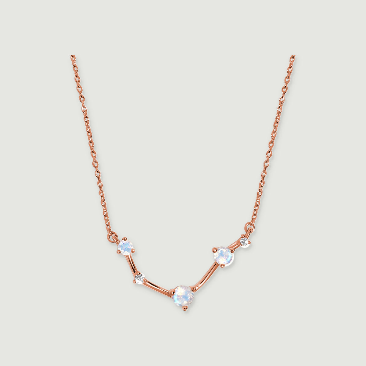 A rose gold necklace displays three round moonstones and two small clear stones joined by polished bars.