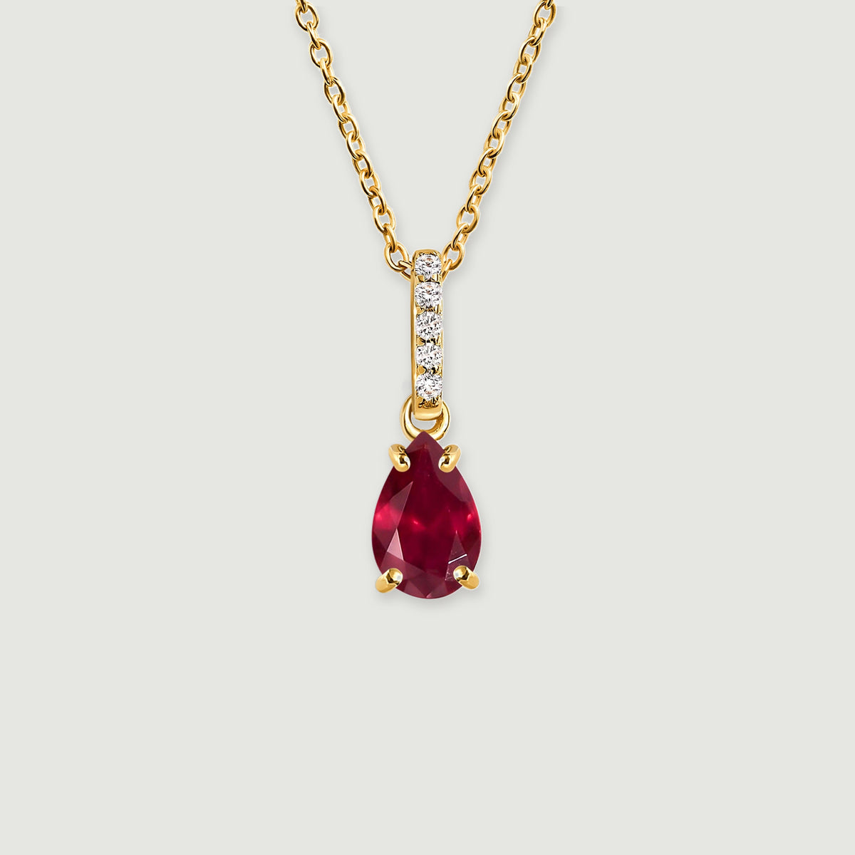 A yellow gold necklace has a pear-shaped red gemstone suspended beneath a vertical row of five clear stones on a light gray background.