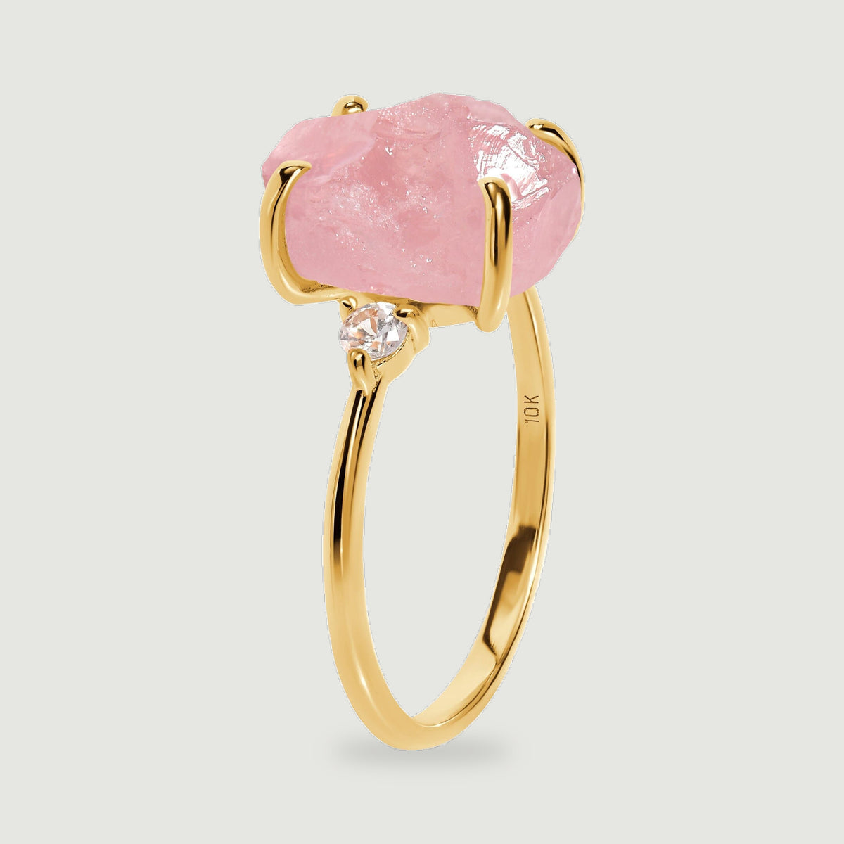 The side of a yellow gold ring shows the raised pink stone, a round clear accent, and the curved band.
