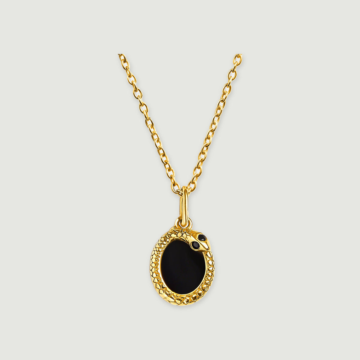 A yellow gold pendant with an oval black stone hangs from a fine link chain on a light gray background.