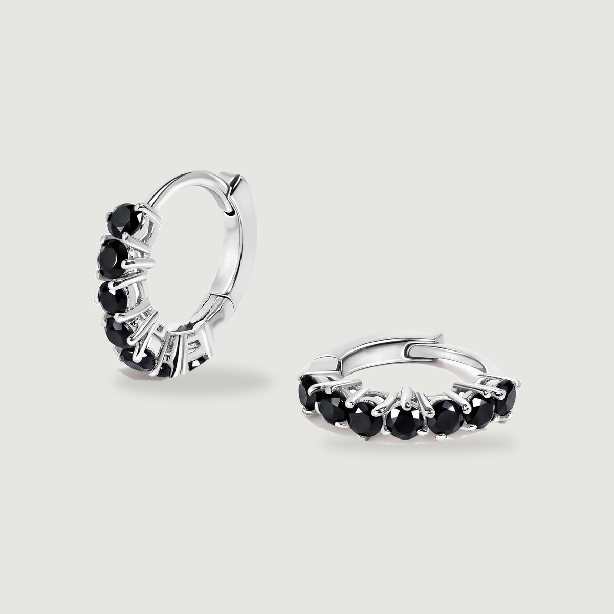 Two silver-colored hoop earrings with round black stones are centered on a light gray surface.