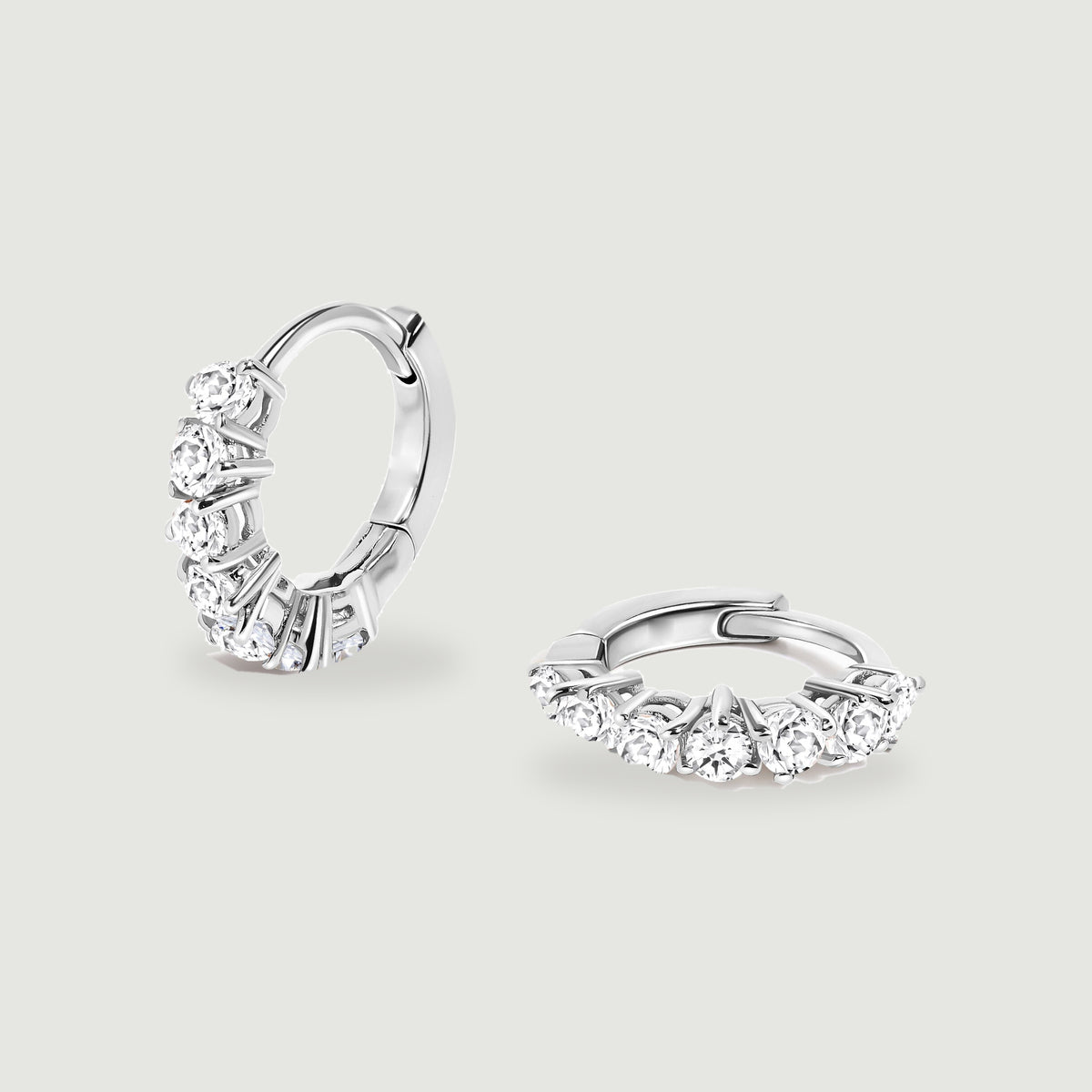 A pair of silver-tone white topaz hoop earrings rests on a light gray surface.