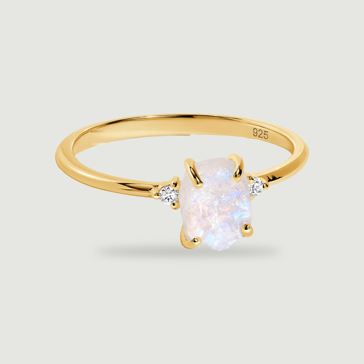 A yellow gold vermeil ring with a pale rough center stone and two small clear stones rests above a soft shadow.