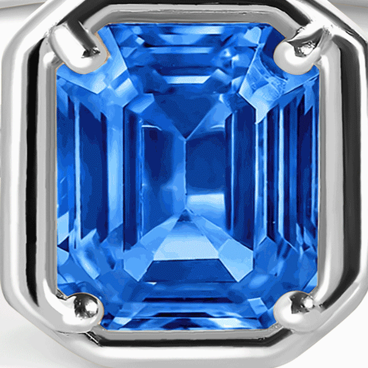 Four silver prongs surround the stepped facets of a rectangular bright blue gemstone.