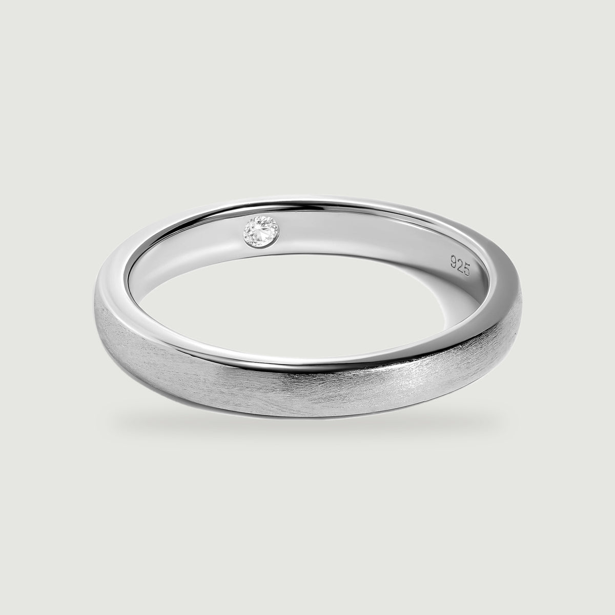 A complete silver ring shows its brushed exterior, polished edges, and a clear round stone inside the band.