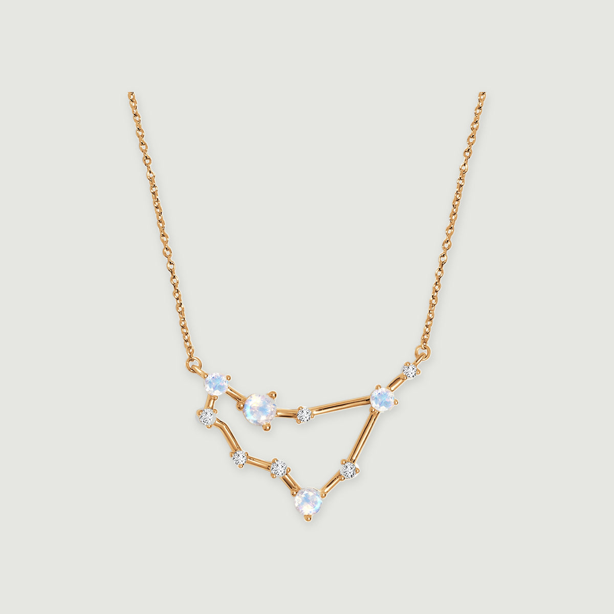 A yellow gold necklace with four pale iridescent stones and smaller clear stones rests against a light gray background.