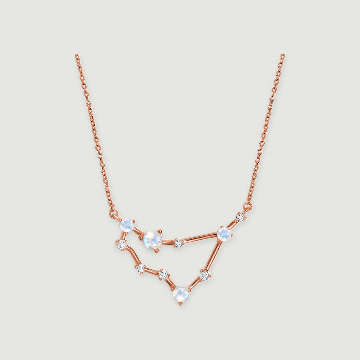 A rose gold necklace shows a fine chain and an angular arrangement of round stones on a light gray surface.
