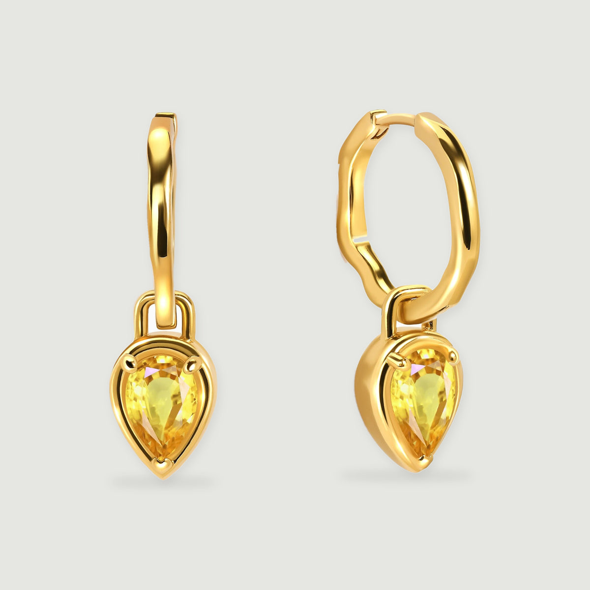A pair of yellow gold plated hoops with pear-shaped yellow citrine drops rests against a light gray background.