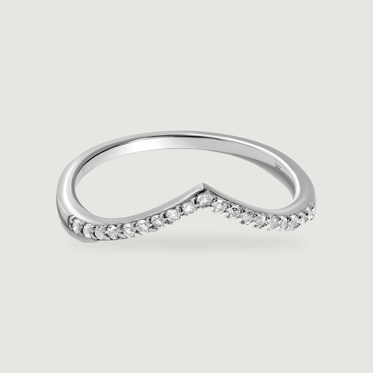 A white gold chevron ring with round diamonds is centered on a pale gray surface.