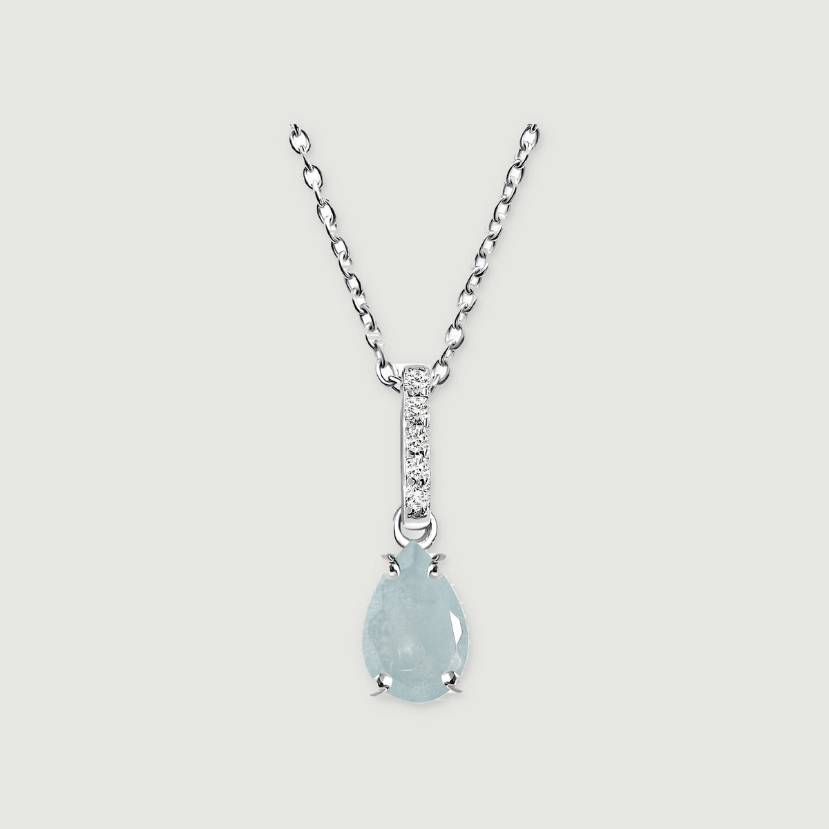 A silver necklace displays a light blue pear-shaped stone held by four prongs on a pale gray surface.