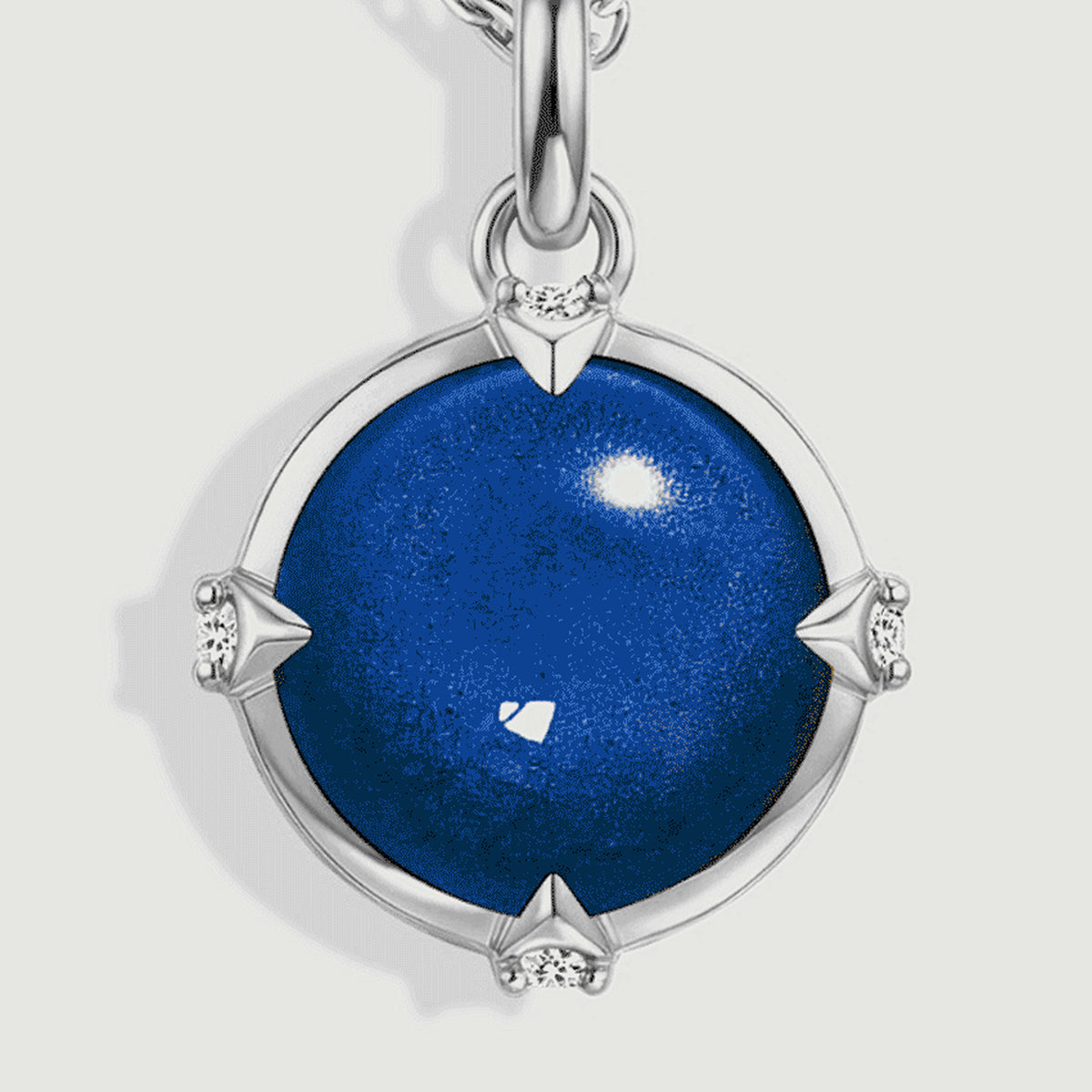 The domed blue cabochon is shown close up with four small clear accents and a polished silver rim.