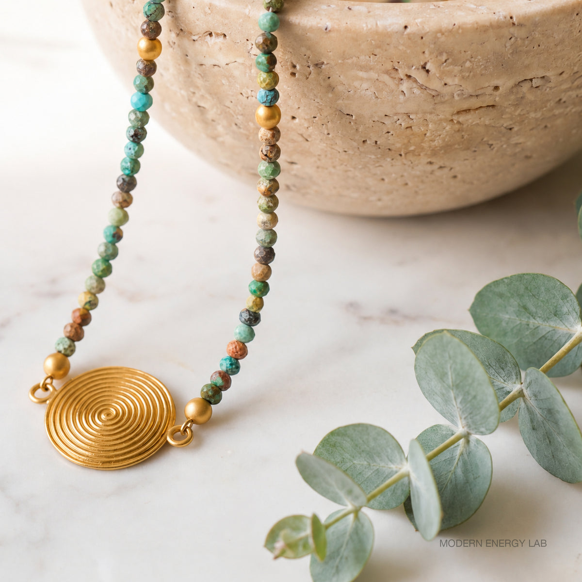 Turquoise necklace beside a pale stone bowl and eucalyptus
