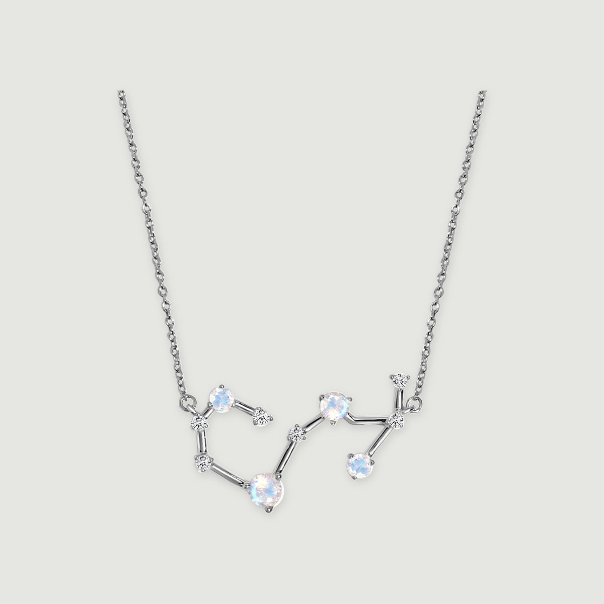 A silver necklace displays a curved constellation pendant with blue-white stones and small clear accents.