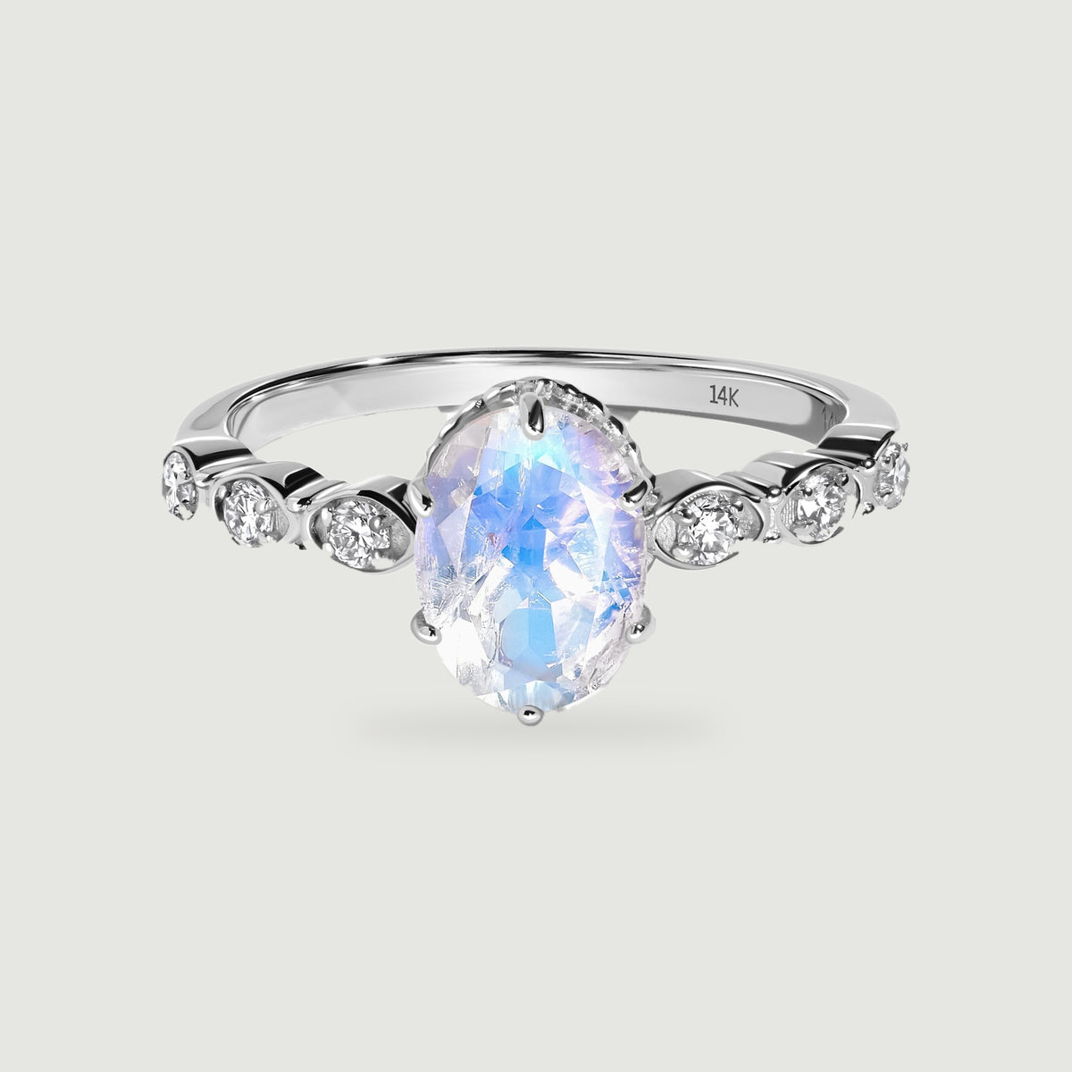 A white gold ring surrounds an oval faceted moonstone with three round diamonds on each shoulder.