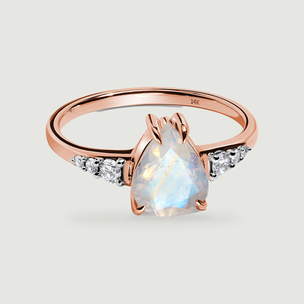 A rose gold ring frames a pale blue pear-shaped stone between two diamond-set shoulders.