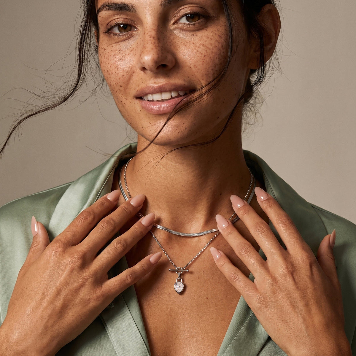 Smiling woman wearing the pear-shaped gemstone necklace, with both hands resting near layered chains.