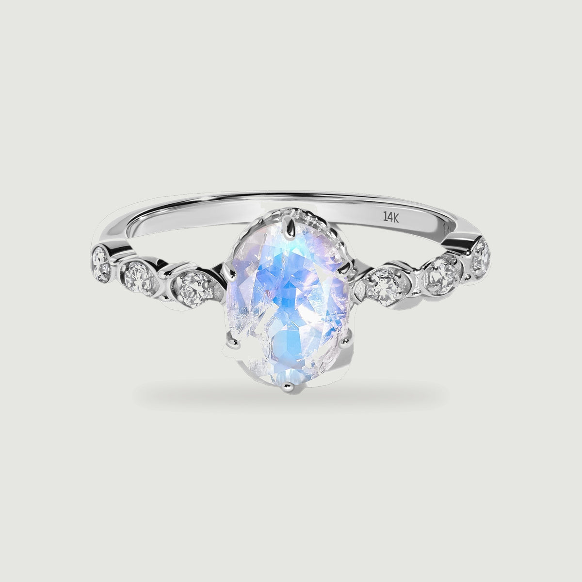 An oval moonstone with blue reflections sits between round diamond accents on a polished white gold ring.