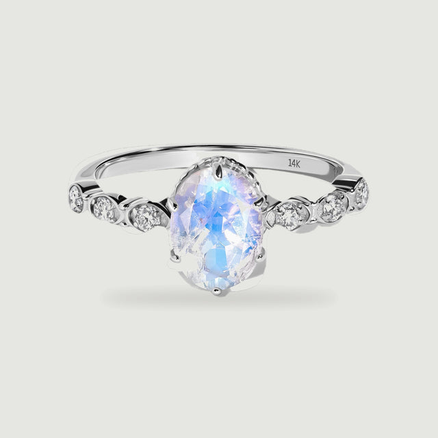 An oval moonstone with blue reflections sits between round diamond accents on a polished white gold ring.