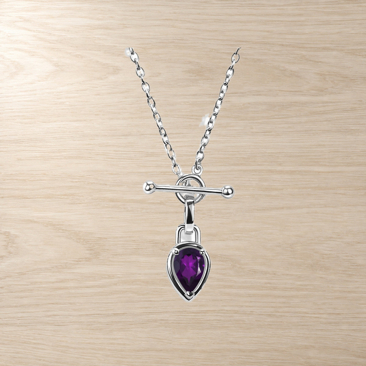 Necklace product closeup showing a faceted purple pear-shaped pendant beneath a horizontal bar clasp.