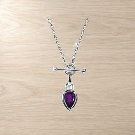 Necklace product closeup showing a faceted purple pear-shaped pendant beneath a horizontal bar clasp.