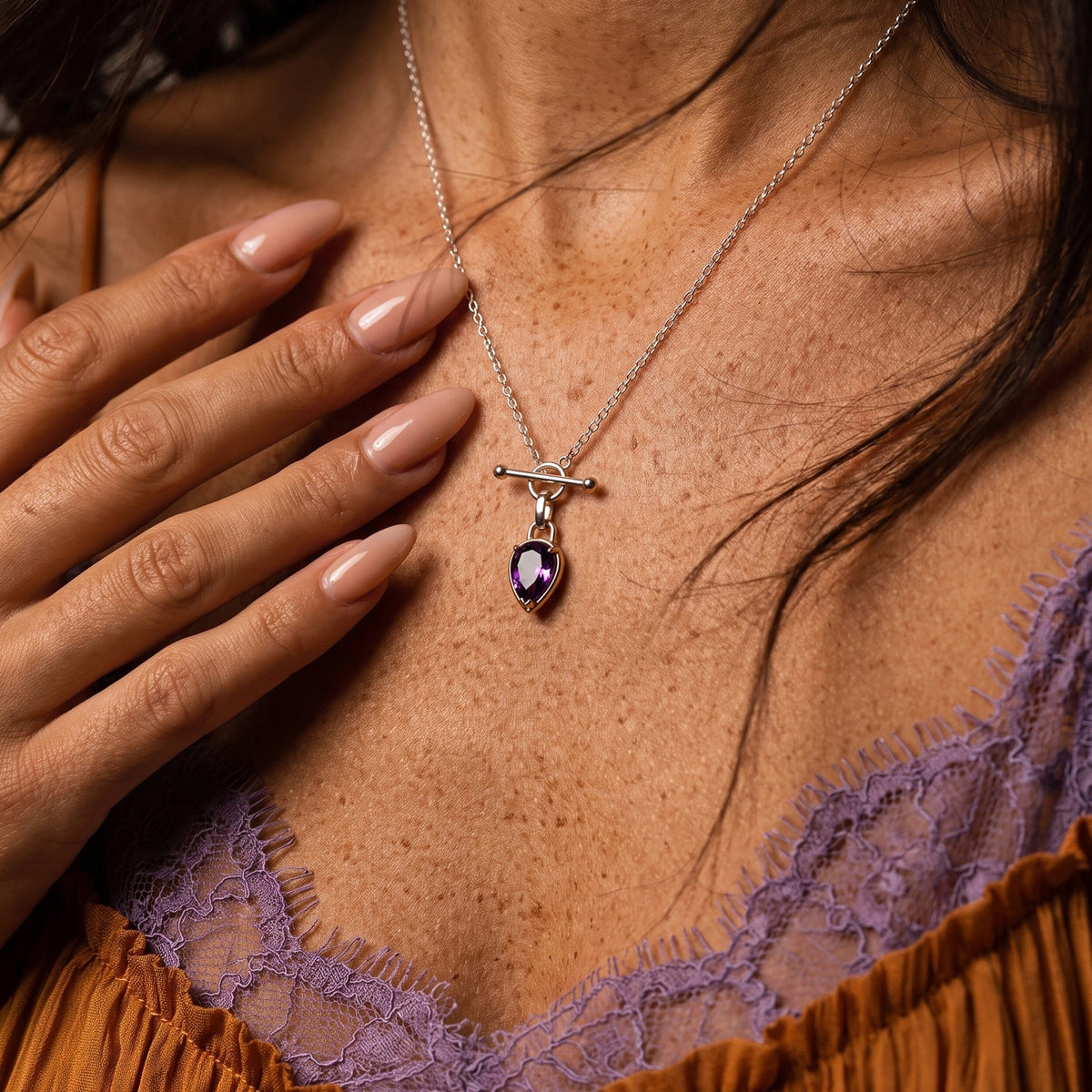 Close-up of a person wearing the necklace, with a purple pear-shaped pendant and hand nearby.