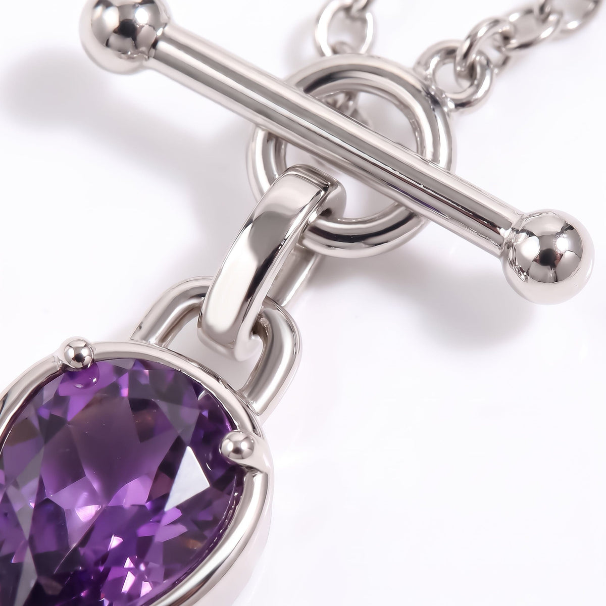 Macro detail of the necklace clasp, chain links, and faceted purple gemstone in a rounded setting.