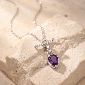 Purple faceted pear-shaped pendant necklace arranged on a textured pale stone surface.