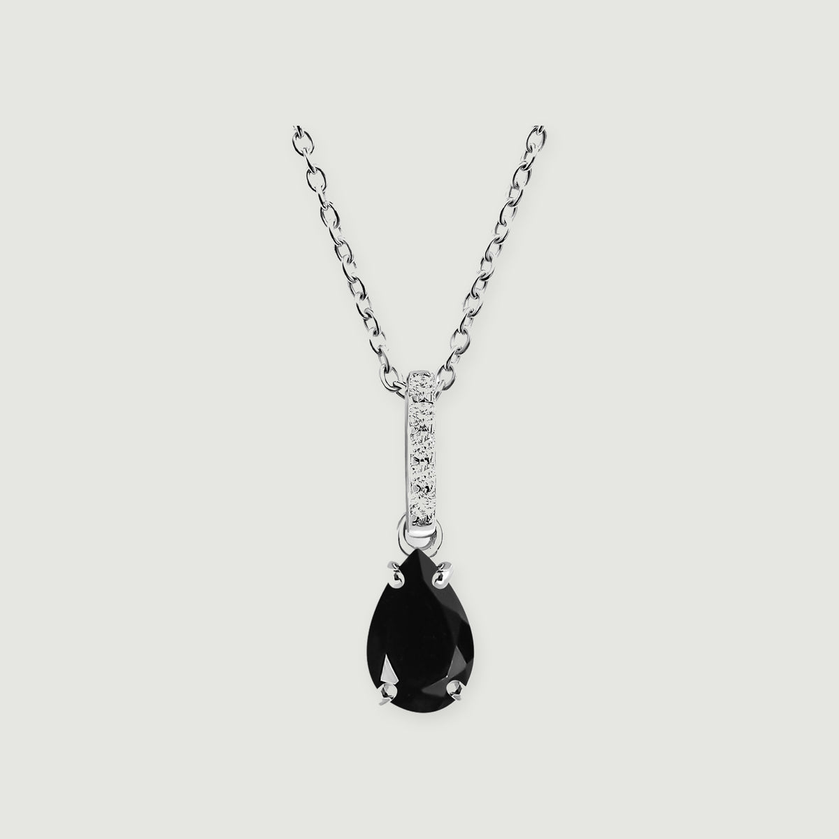 A sterling silver chain holds a pear-shaped black onyx pendant below a narrow diamond-set bail on a light gray background.