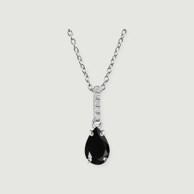 A sterling silver chain holds a pear-shaped black onyx pendant below a narrow diamond-set bail on a light gray background.