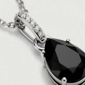 A close view shows the silver prongs, black onyx facets, and round diamonds along the pendant bail.