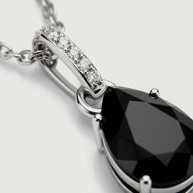 A close view shows the silver prongs, black onyx facets, and round diamonds along the pendant bail.