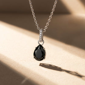 A silver black onyx necklace casts a long angled shadow across a pale stone surface.